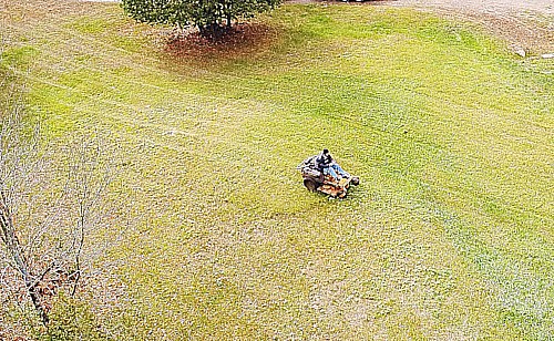 a Zero point turn tractor cutting on a front lawn image shot from a drone